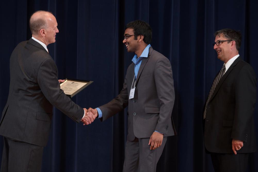 Award recipient in a grey suit smiling and shaking hands with Doctor Potteiger